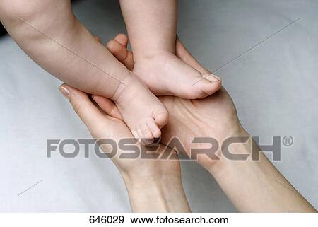 Stock Photo - Close up of mother holding newborn’s feet. Fotosearch