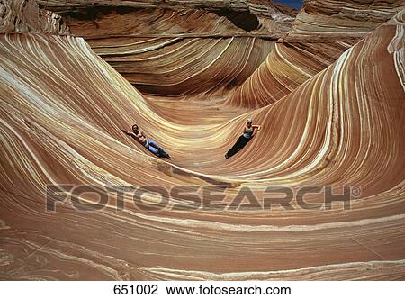 Stock Image - Two People lie in The Wave, Coyote Buttes, Paria Canyon-Vermilion Cliffs Wilderness, Arizona, USA. Fotosearch