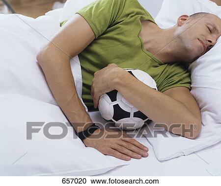 Stock Image - A man sleeping in bed with a football. Fotosearch