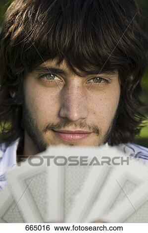 Stock Photograph - A man looking from behind a hand of cards. Fotosearch