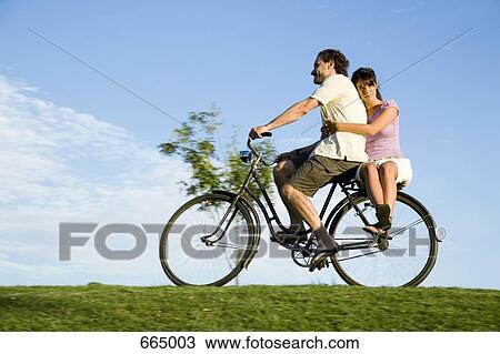 A man riding a bicycle and a young woman sitting on the back View Large Photo Image Stock Image - A man riding a bicycle and a young woman sitting on the back. Fotosearch