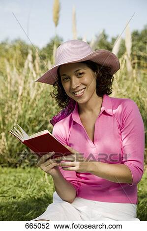 A woman sitting and reading a book on grass View Large Photo Image Stock Image - A woman sitting and reading a book on grass. Fotosearch