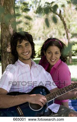 A young couple sitting underneath a tree and playing a guitar View Large Photo Image Stock Image - A young couple sitting underneath a tree and playing a guitar. Fotosearch