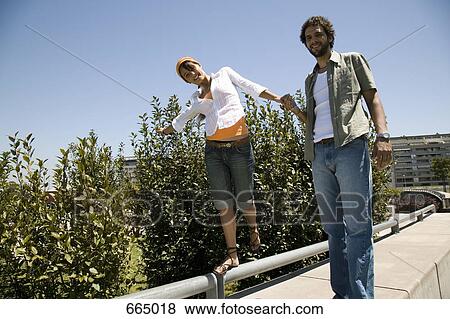 Stock Photo - A young couple walking along a wall and holding hands. Fotosearch