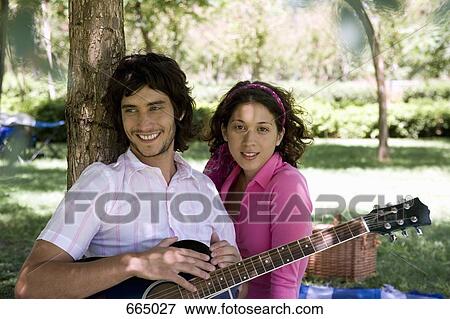 A young man and woman sitting underneath a tree with a guitar View Large Photo Image Stock Photo - A young man and woman sitting underneath a tree with a guitar. Fotosearch