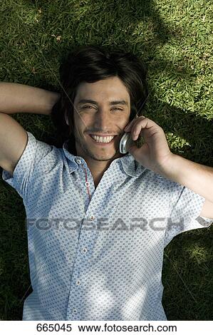 A young man lying on grass and using his mobile phone View Large Photo Image Stock Photography - A young man lying on grass and using his mobile phone. Fotosearch