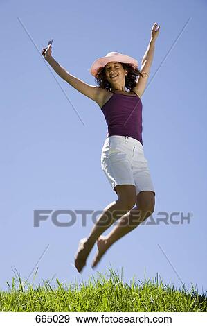 A young woman leaping in the air and holding a mobile phone View Large Photo Image Stock Photo - A young woman leaping in the air and holding a mobile phone. Fotosearch