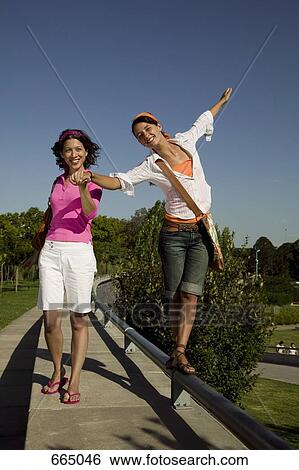 Two young women walking on top of a wall and holding hands View Large Photo Image Stock Photograph - Two young women walking on top of a wall and holding hands. Fotosearch