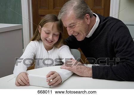 A granddaughter using a electronic device while her grandfather watch View Large Photo Image Stock Image - A granddaughter using a electronic device while her grandfather watch. Fotosearch