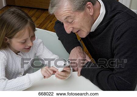 A granddaughter using a electronic device while her grandfather watch View Large Photo Image Stock Image - A granddaughter using a electronic device while her grandfather watch. Fotosearch