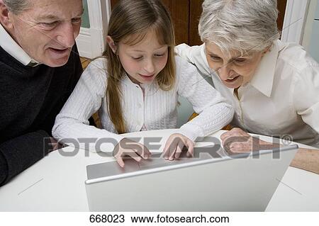 Stock Image - A granddaughter using a laptop while her grandparents watch. Fotosearch