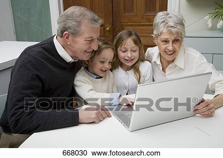 Stock Image - Grandchildren using a laptop while their grandparents watch. Fotosearch