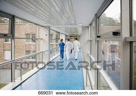 Stock Image - Three healthcare workers walking along a corridor. Fotosearch