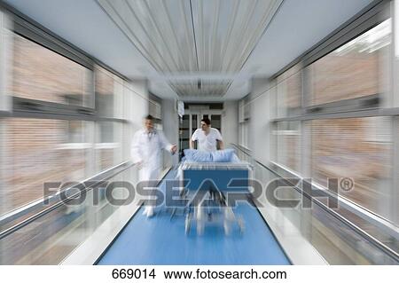 Two healthcare workers pushing a hospital bed along a corridor View Large Photo Image Picture - Two healthcare workers pushing a hospital bed along a corridor. Fotosearch