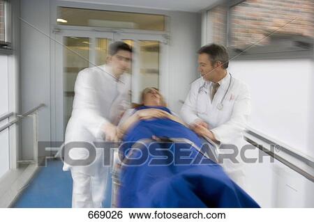 Two healthcare workers pushing a patient along a corridor View Large Photo Image Stock Photograph - Two healthcare workers pushing a patient along a corridor. Fotosearch