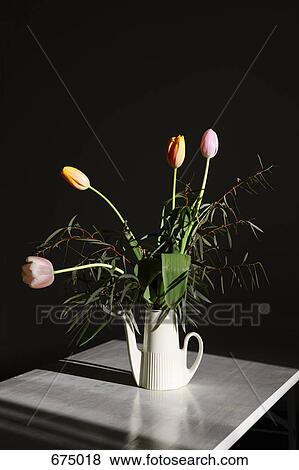 Stock Photo - A bouquet of tulips in a watering can on a table, still life. Fotosearch