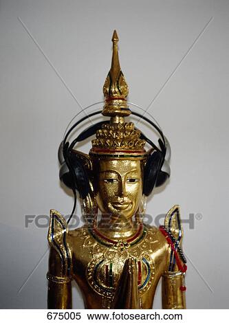 Stock Photography - A praying gold Buddha statue with headphones on. Fotosearch