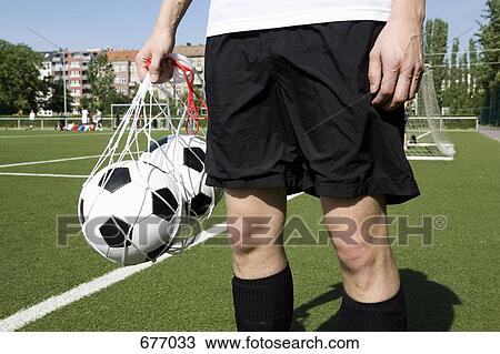 A young man carrying two soccer balls in a net, mid View Large Photo Image Stock Image - A young man carrying two soccer balls in a net, mid. Fotosearch