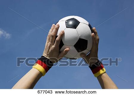 Stock Image - Hands holding a soccer ball in the air. Fotosearch