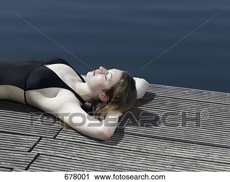 A woman in a swimsuit lying on a jetty View Large Photo Image Stock Image - A woman in a swimsuit lying on a jetty. Fotosearch