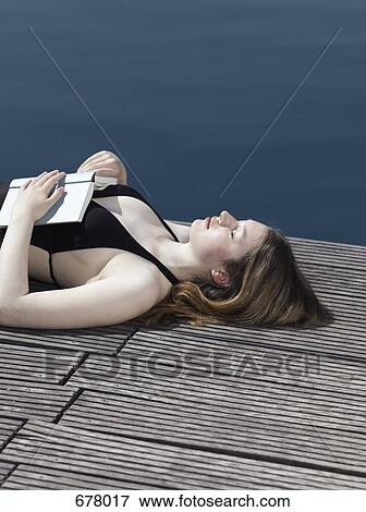 A woman lying on a jetty with an open book on her chest View Large Photo Image Stock Photo - A woman lying on a jetty with an open book on her chest. Fotosearch