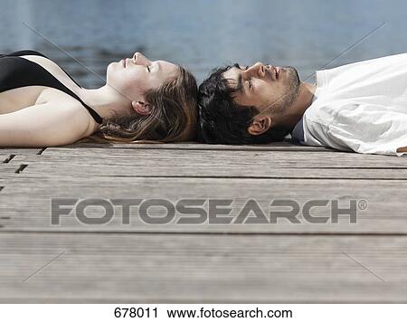 A young couple lying on a jetty head to head View Large Photo Image Stock Image - A young couple lying on a jetty head to head. Fotosearch