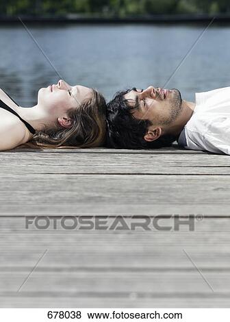 A young couple lying on a jetty head to head View Large Photo Image Stock Photo - A young couple lying on a jetty head to head. Fotosearch