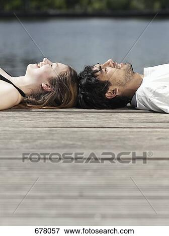 A young couple lying on a jetty head to head View Large Photo Image Stock Photo - A young couple lying on a jetty head to head. Fotosearch