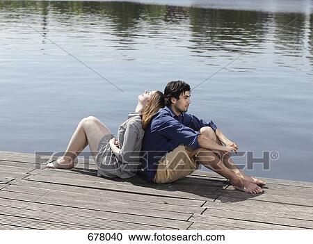 A young couple sitting back to back on a jetty View Large Photo Image Stock Image - A young couple sitting back to back on a jetty. Fotosearch