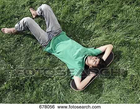A young man lying in the grass with his head on a skateboard View Large Photo Image Stock Photograph - A young man lying in the grass with his head on a skateboard. Fotosearch