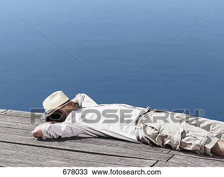 Stock Image - A young man lying on a jetty. Fotosearch