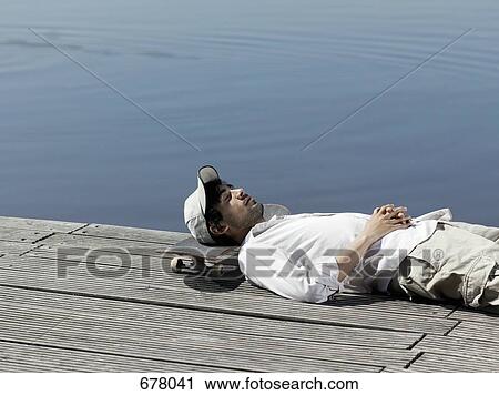 Stock Image - A young man resting his head on a skateboard on a jetty. Fotosearch