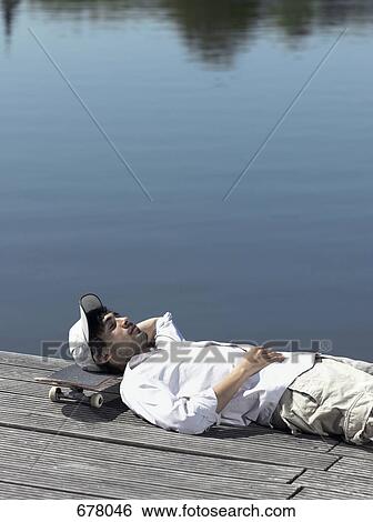 A young man resting his head on a skateboard on a jetty View Large Photo Image Stock Photograph - A young man resting his head on a skateboard on a jetty. Fotosearch