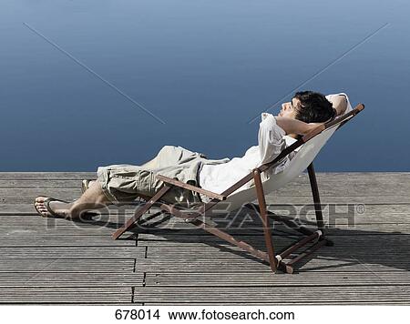 A young man sitting in a deck chair on a jetty View Large Photo Image Picture - A young man sitting in a deck chair on a jetty. Fotosearch