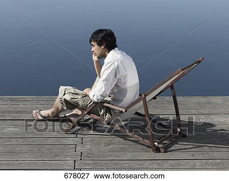 A young man sitting in a deck chair on a jetty talking on a mobile phone View Large Photo Image Stock Photo - A young man sitting in a deck chair on a jetty talking on a mobile phone. Fotosearch