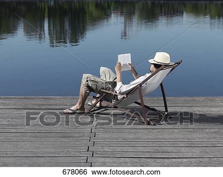 A young man sitting in a deck chair on a jetty reading a book View Large Photo Image Stock Photograph - A young man sitting in a deck chair on a jetty reading a book. Fotosearch