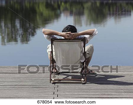 Picture - Rear view of a man sitting in a deck chair on a jetty. Fotosearch