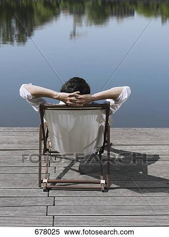Stock Photography - Rear view of a man sitting in a deck chair on a jetty. Fotosearch
