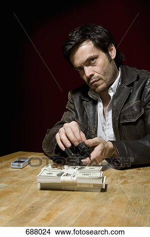 A man loading a gun with bullets next to several stacks of money View Large Photo Image Picture - A man loading a gun with bullets next to several stacks of money. Fotosearch