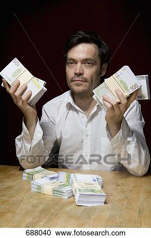 A man sitting at a table with bundles of hundred euro banknotes View Large Photo Image Stock Image - A man sitting at a table with bundles of hundred euro banknotes. Fotosearch