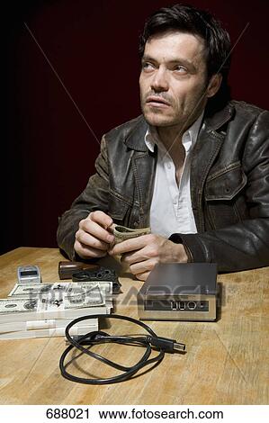 A man sitting at a table with stacks of money, a mobile phone and a hard drive View Large Photo Image Stock Image - A man sitting at a table with stacks of money, a mobile phone and a hard drive. Fotosearch