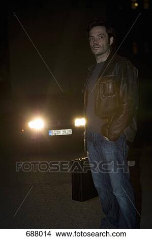 Picture - A man standing in front of headlights with a briefcase. Fotosearch