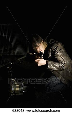 Stock Image - A man with a nylon over his face aiming a gun with a briefcase full of money. Fotosearch