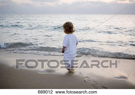 Stock Image - A boy walking on the beach at dusk. Fotosearch