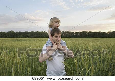 Stock Image - A man carrying a child on his shoulders through a wheat field. Fotosearch