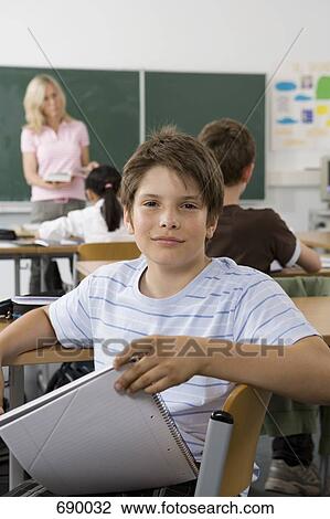 Stock Image - A pre-adolescent boy sitting in the back of a classroom, looking at camera. Fotosearch