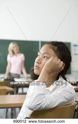 Stock Image - A pre-adolescent girl sitting in the back of a classroom looking bored. Fotosearch