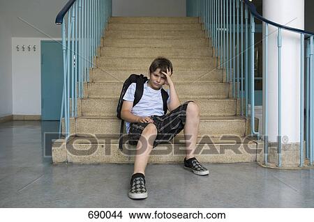 A worried pre-adolescent boy sitting on stairs in a school View Large Photo Image Picture - A worried pre-adolescent boy sitting on stairs in a school. Fotosearch
