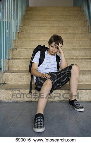 Stock Photograph - A worried pre-adolescent boy sitting on stairs in a school. Fotosearch