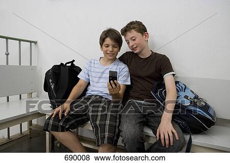 Two pre-adolescent boys sitting on a bench looking at a mobile phone View Large Photo Image Stock Photo - Two pre-adolescent boys sitting on a bench looking at a mobile phone. Fotosearch